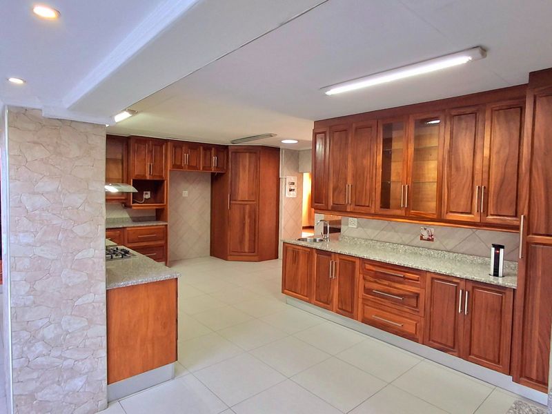 Spacious kitchen featuring extensive wooden cabinetry, granite countertops, built-in oven, gas hob, and a decorative stone-clad pillar, offering ample storage and workspace.
