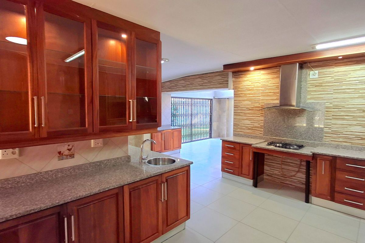 Spacious kitchen featuring warm wooden cabinetry, granite countertops, a built-in gas hob with extractor fan, and neutral floor tiling.