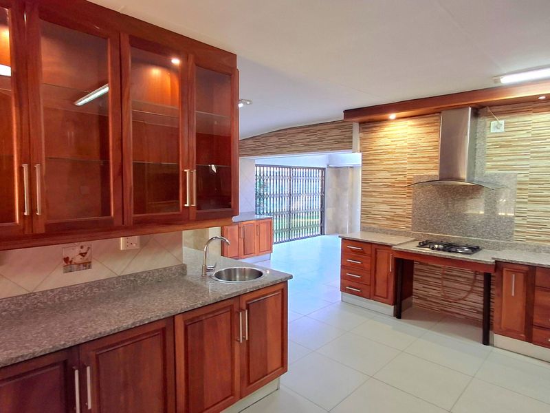 Spacious kitchen featuring warm wooden cabinetry, granite countertops, a built-in gas hob with extractor fan, and neutral floor tiling.