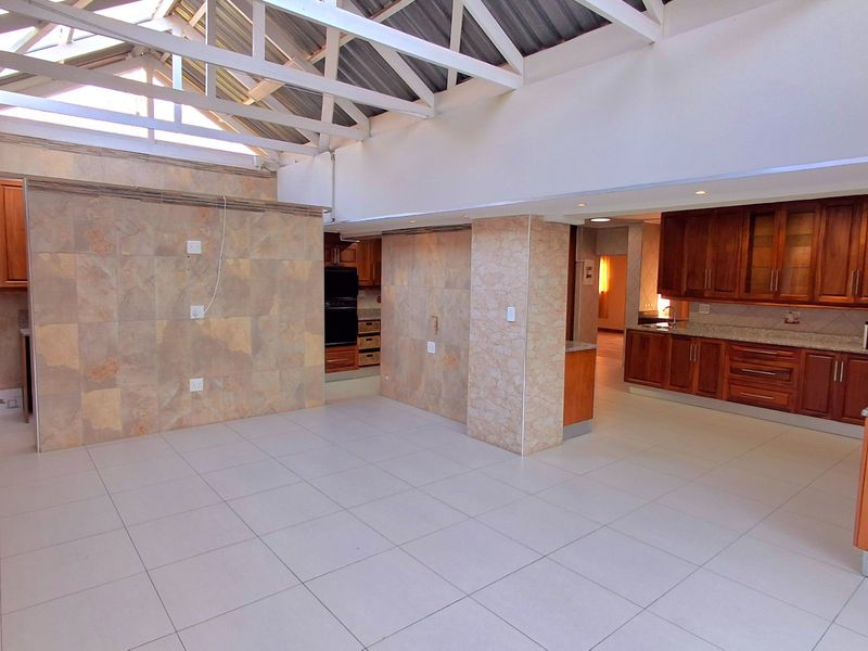 Spacious open-plan living area featuring high ceilings with exposed trusses, stone-clad feature walls, and a well-appointed kitchen with granite countertops and wooden cabinetry.