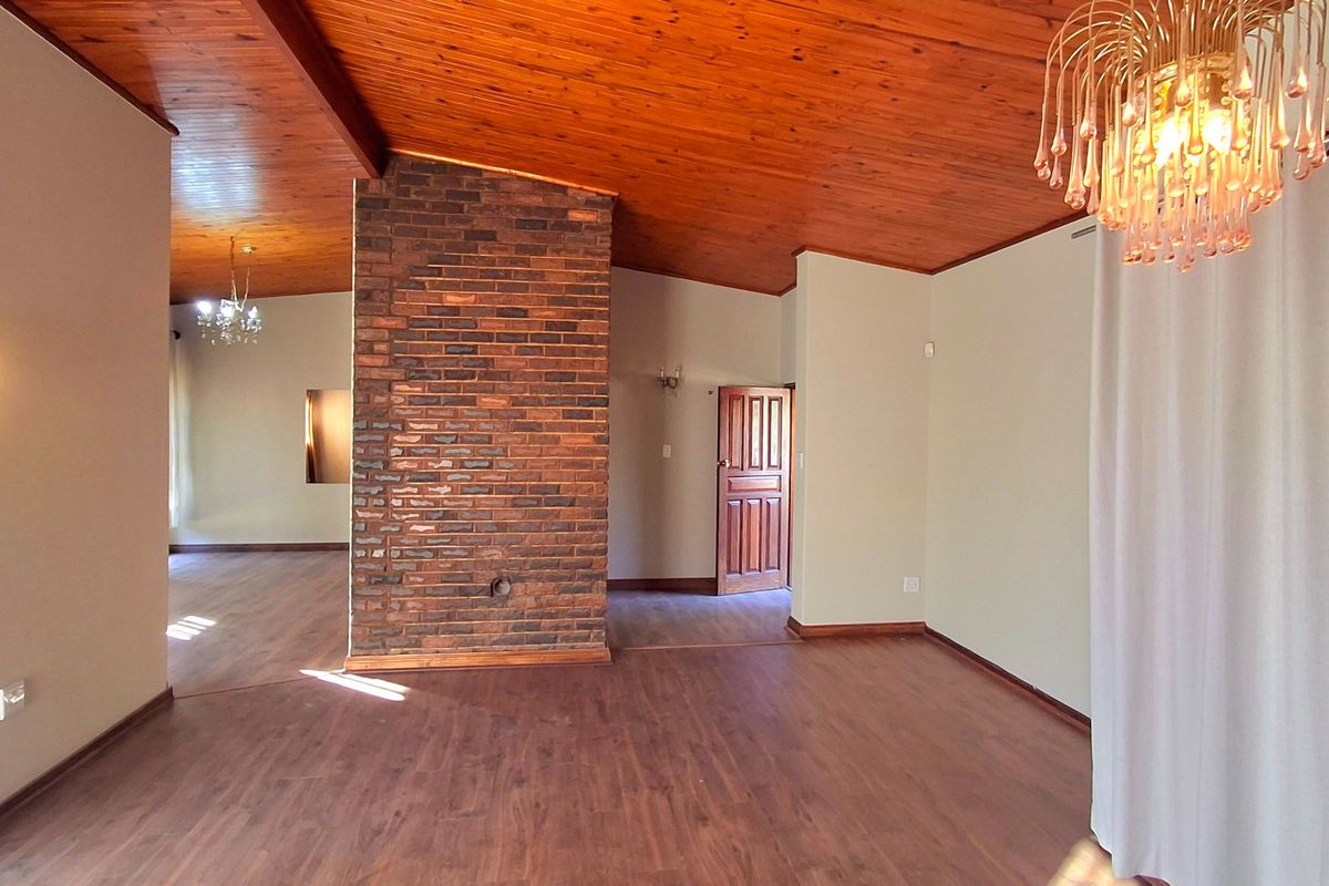 Spacious living area featuring a prominent exposed brick fireplace, warm timber tongue and groove ceilings, and durable laminate flooring throughout.