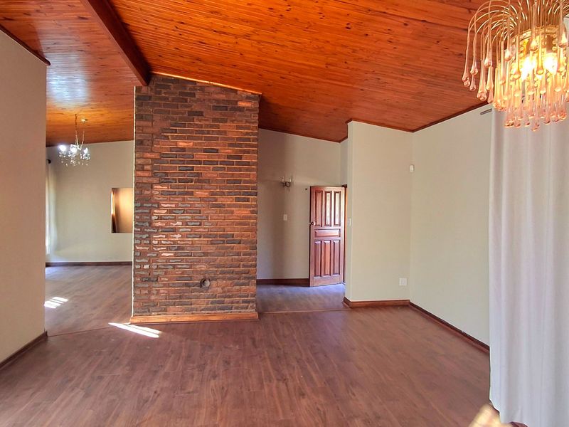 Spacious living area featuring a prominent exposed brick fireplace, warm timber tongue and groove ceilings, and durable laminate flooring throughout.