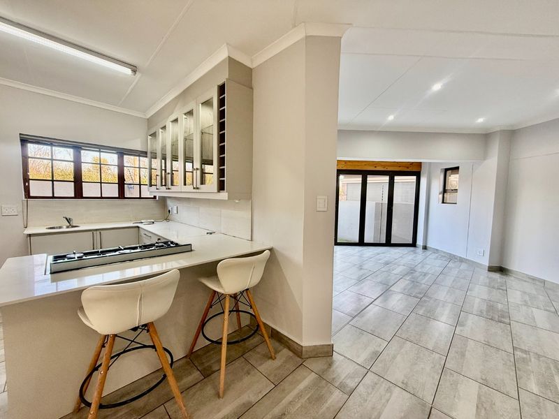Modern open-plan kitchen and living area featuring sleek cabinetry, stone countertops, a gas hob, and large sliding doors leading to the exterior.