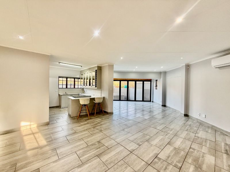 Spacious open-plan living area featuring modern tiled flooring, a functional kitchen with island, and large aluminium stacker doors leading to the outdoor space.