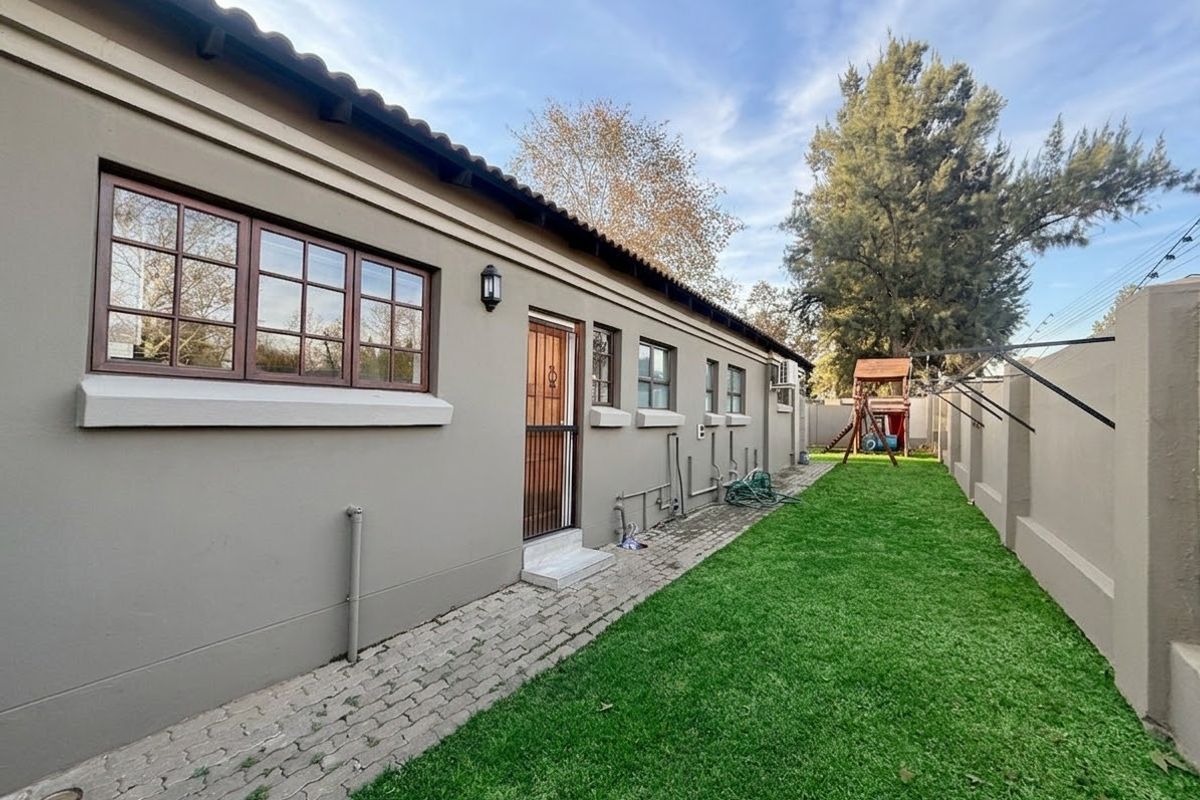 Rear exterior view of the house featuring a paved walkway, well-maintained lawn, boundary wall, and timber-framed windows.