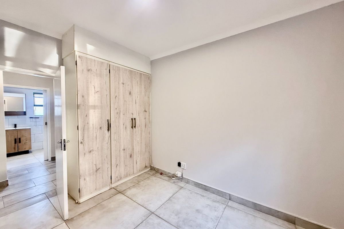 A bright, empty bedroom featuring neutral tiled flooring, a built-in wardrobe with wood-grain finish, and a view into the adjacent bathroom.