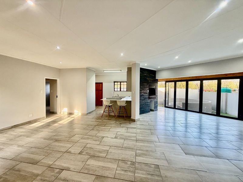 Spacious open-plan living area featuring large format floor tiles, a modern stone-clad fireplace, and bi-fold doors opening to the outdoor space.