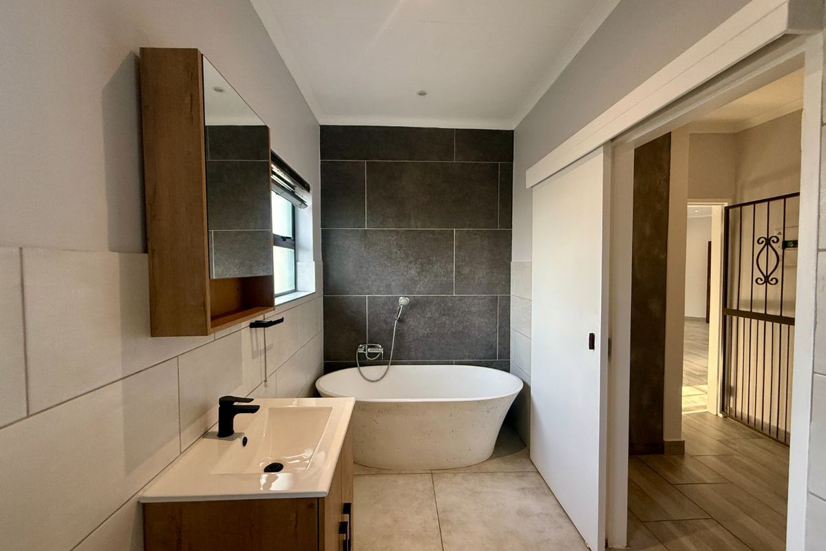 Modern bathroom featuring a freestanding bathtub, dark tiled feature wall, vanity with basin, and a sliding door entry.