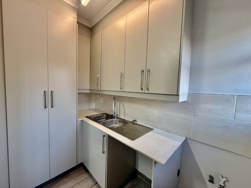 A clean and functional laundry area featuring built-in cabinetry, a stainless steel sink, and tiled backsplash with dedicated plumbing connections.
