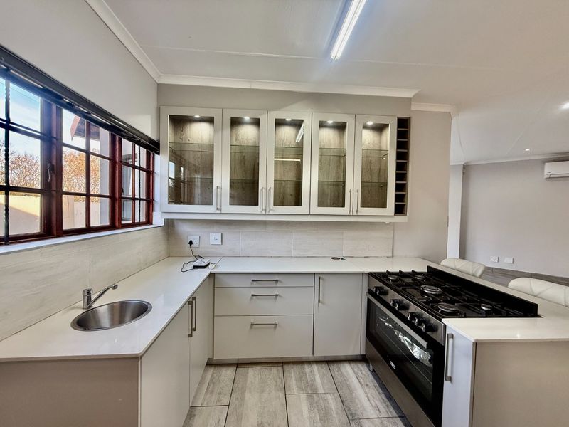 Modern kitchen featuring white cabinetry, stone countertops, glass-fronted display units, a gas hob, and integrated oven with tiled flooring.