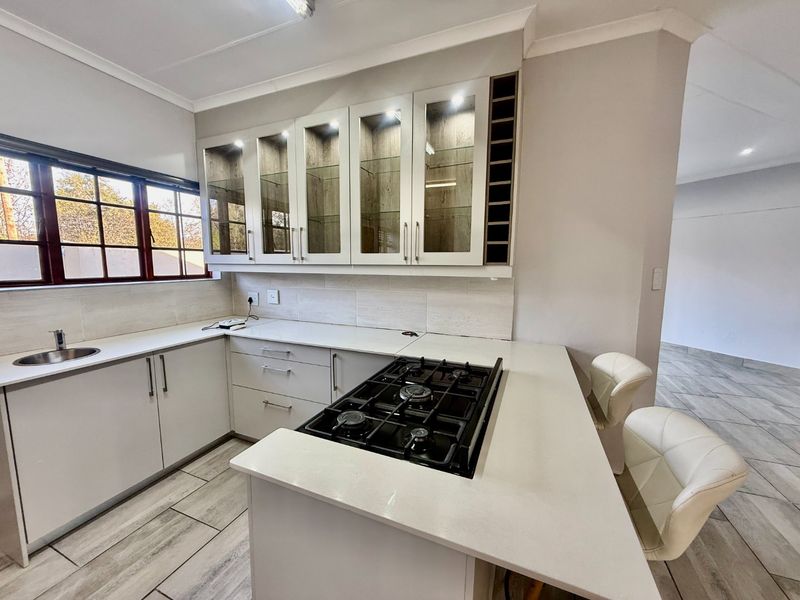 Modern kitchen featuring white cabinetry, stone countertops, a gas hob, and glass-fronted display units with integrated lighting.