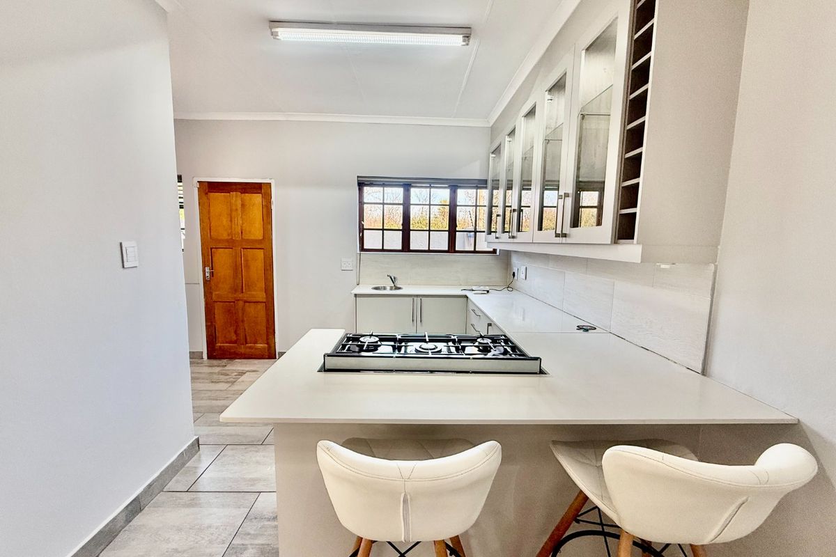 Modern kitchen featuring stone countertops, a built-in gas hob, ample cabinetry with glass-fronted display units, and tiled flooring.