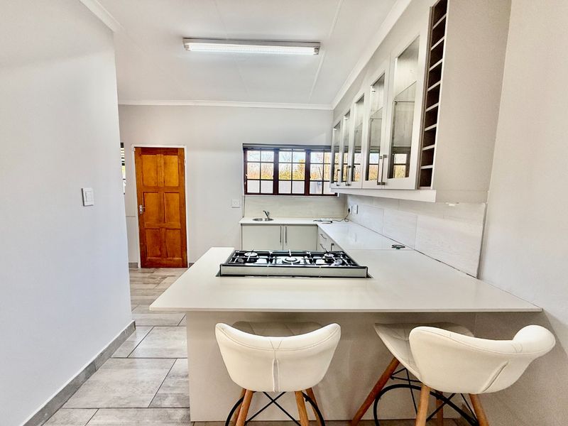 Modern kitchen featuring stone countertops, a built-in gas hob, ample cabinetry with glass-fronted display units, and tiled flooring.