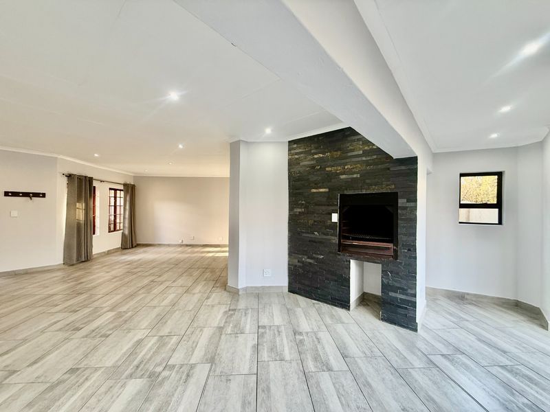 Spacious open-plan living area featuring a modern stone-clad indoor braai, neutral tiled flooring, and recessed downlighting throughout the bright, airy space.