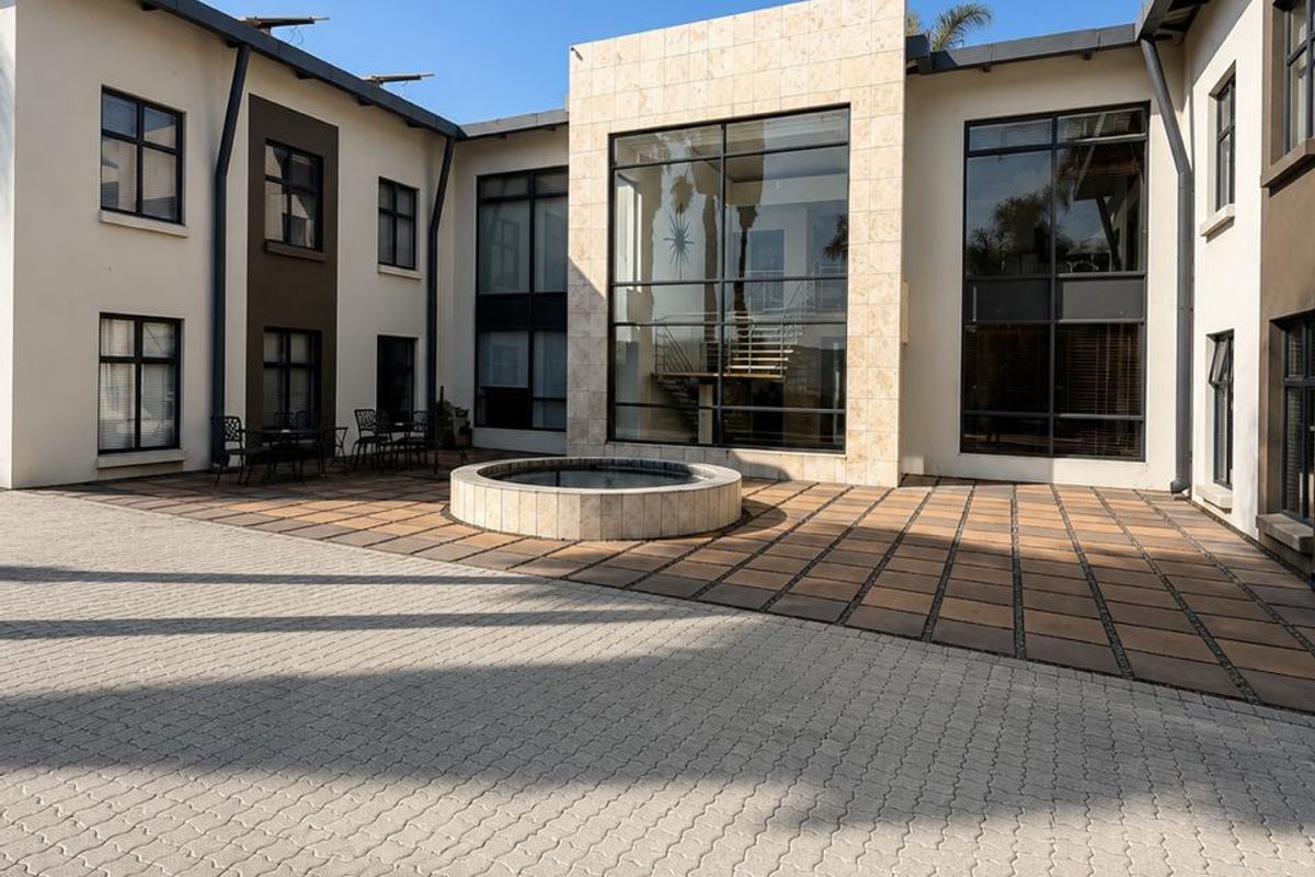 A well-maintained commercial courtyard featuring a central water feature, stone-clad architectural accents, and extensive glass paneling providing natural light to the interior.