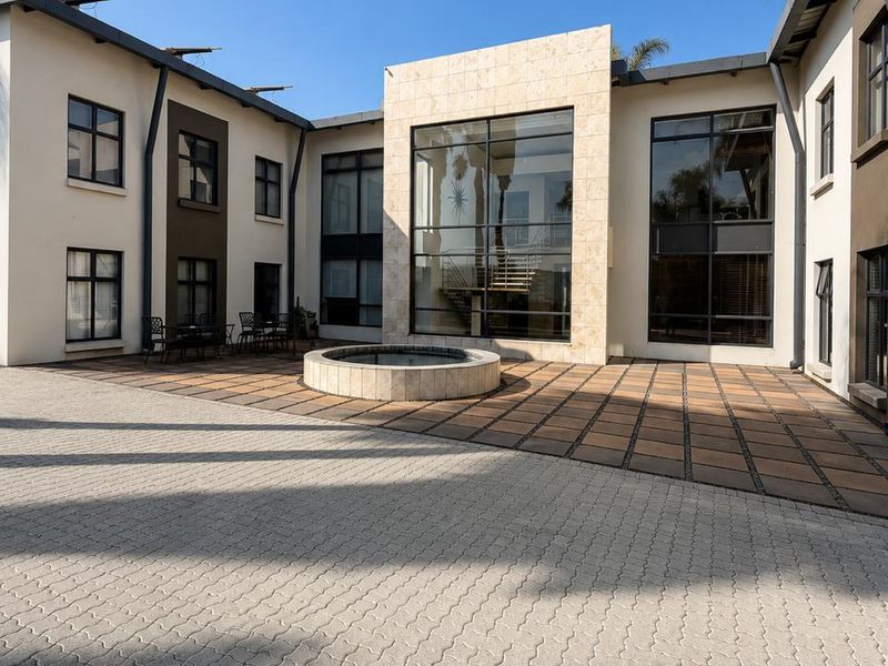 A well-maintained commercial courtyard featuring a central water feature, stone-clad architectural accents, and extensive glass paneling providing natural light to the interior.