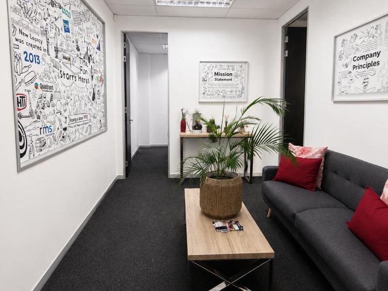 A professional office hallway featuring dark carpeting, recessed ceiling lighting, and clean white walls, providing a functional and well-maintained transition space.