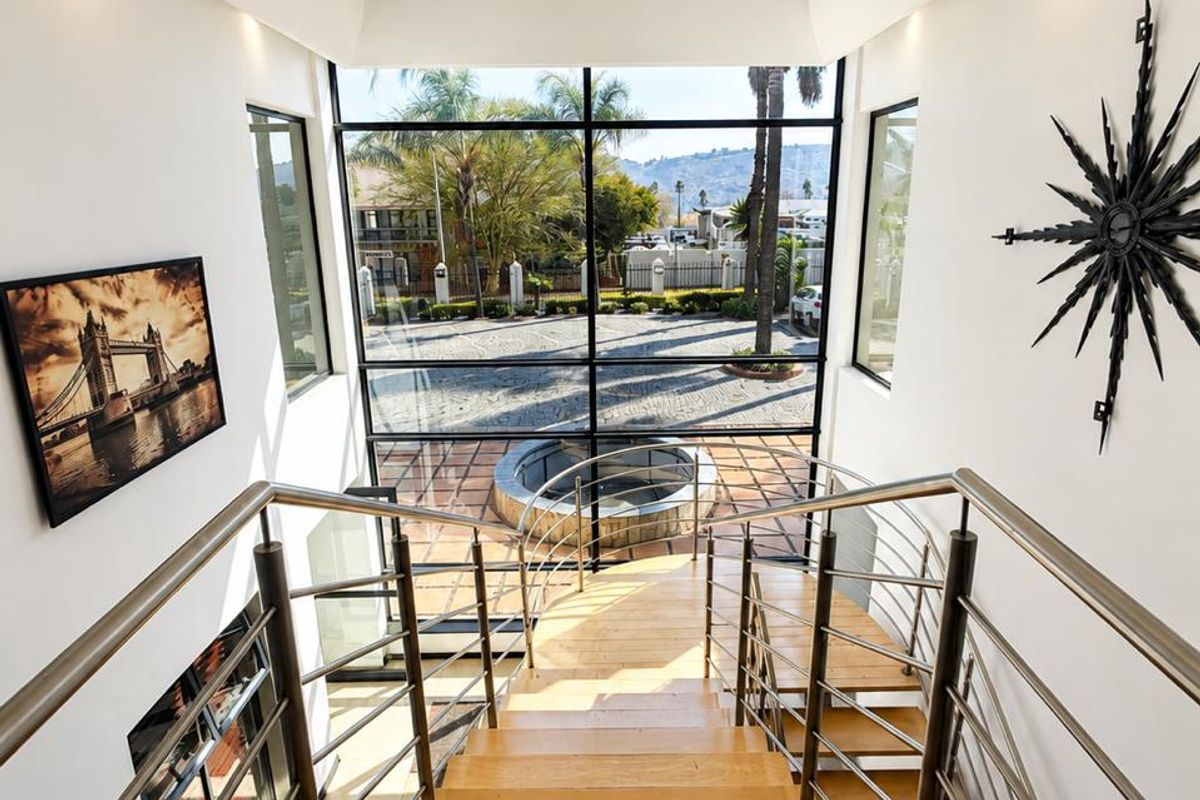 A bright, modern entrance featuring a timber staircase with stainless steel balustrades and a large floor-to-ceiling glass window overlooking the exterior courtyard.