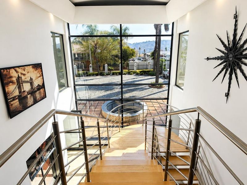 A bright, modern entrance featuring a timber staircase with stainless steel balustrades and a large floor-to-ceiling glass window overlooking the exterior courtyard.