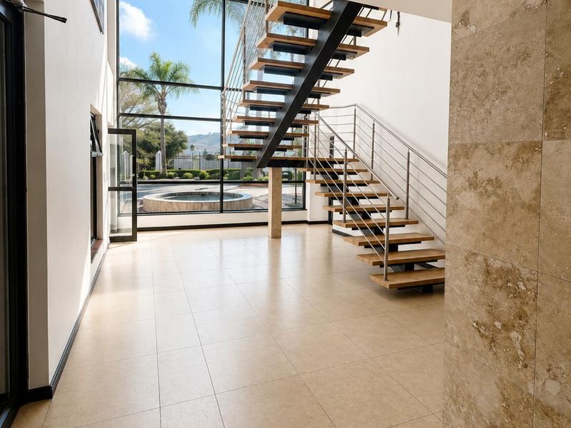 Spacious modern entrance hall featuring a striking floating staircase, floor-to-ceiling windows with garden views, and elegant travertine wall accents.