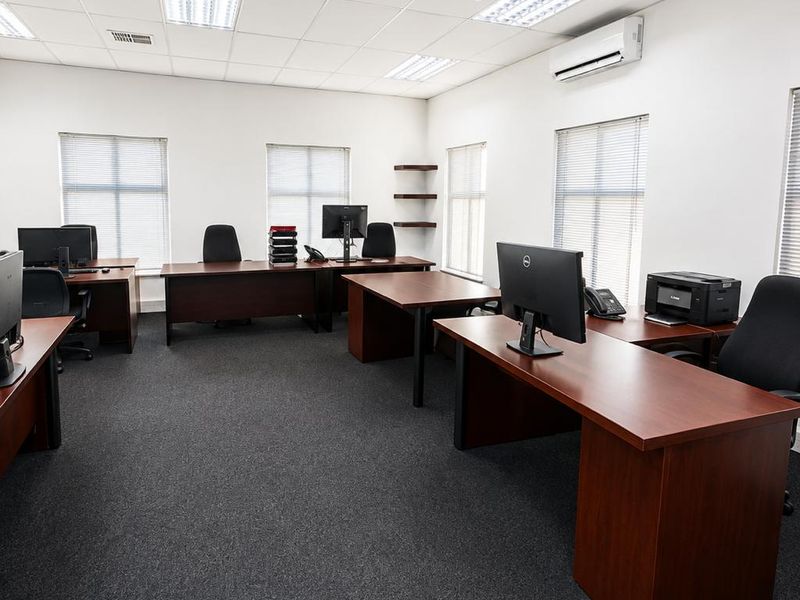 A professional commercial office space featuring a suspended ceiling, recessed lighting, split-system air conditioning, and carpeted flooring with multiple workstations.