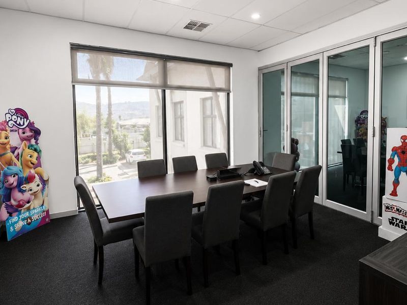 A professional meeting room featuring a large conference table, glass partition walls, recessed lighting, and a suspended ceiling system.