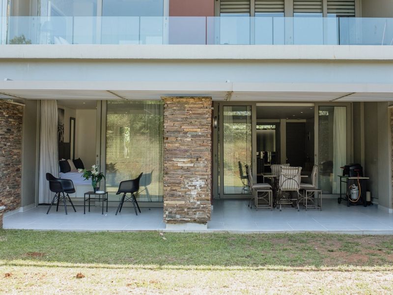 A spacious covered patio featuring stone-clad pillars, tiled flooring, and large sliding glass doors providing seamless indoor-outdoor flow.