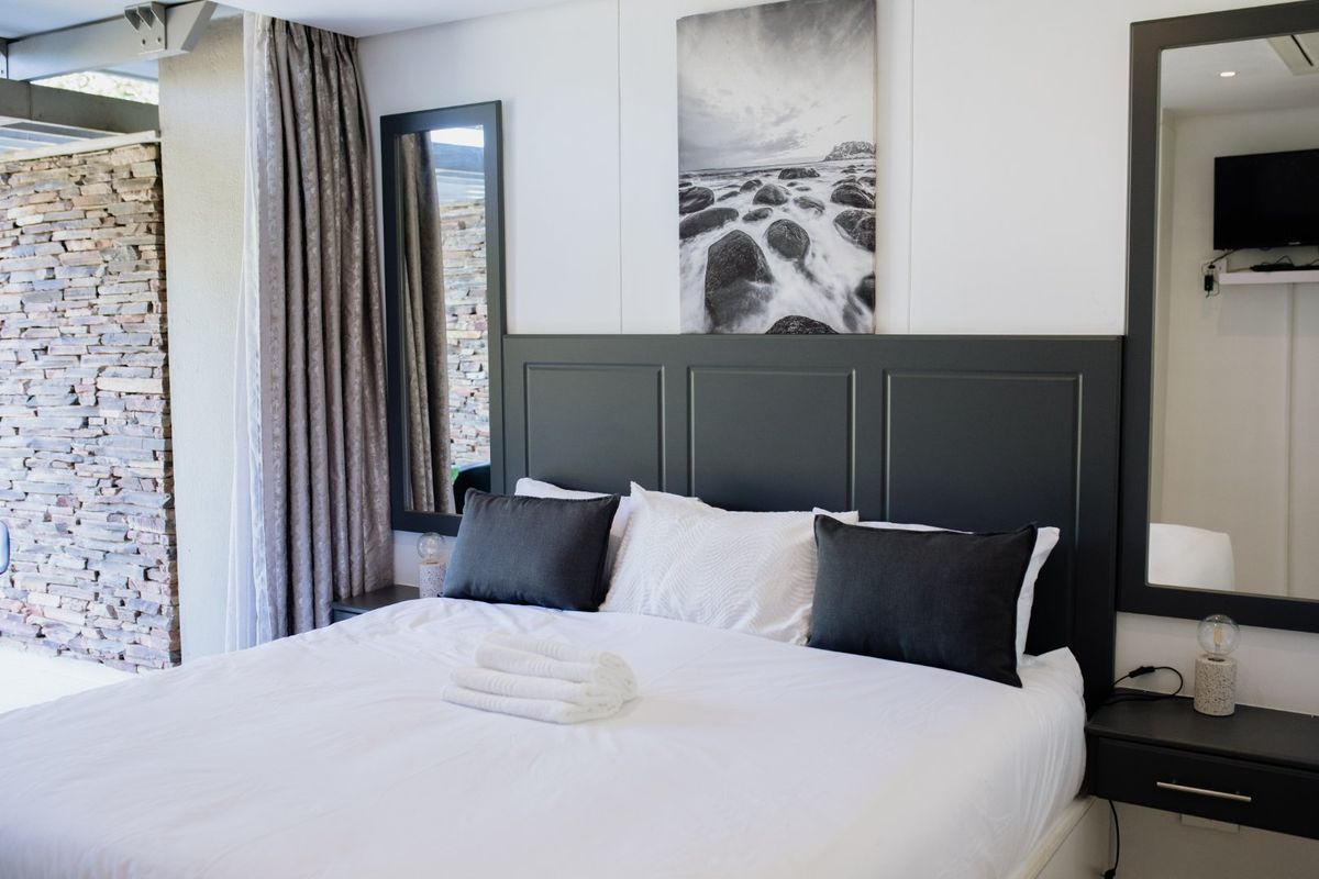 A well-appointed bedroom featuring a dark built-in headboard, integrated bedside tables, and a striking stone feature wall.