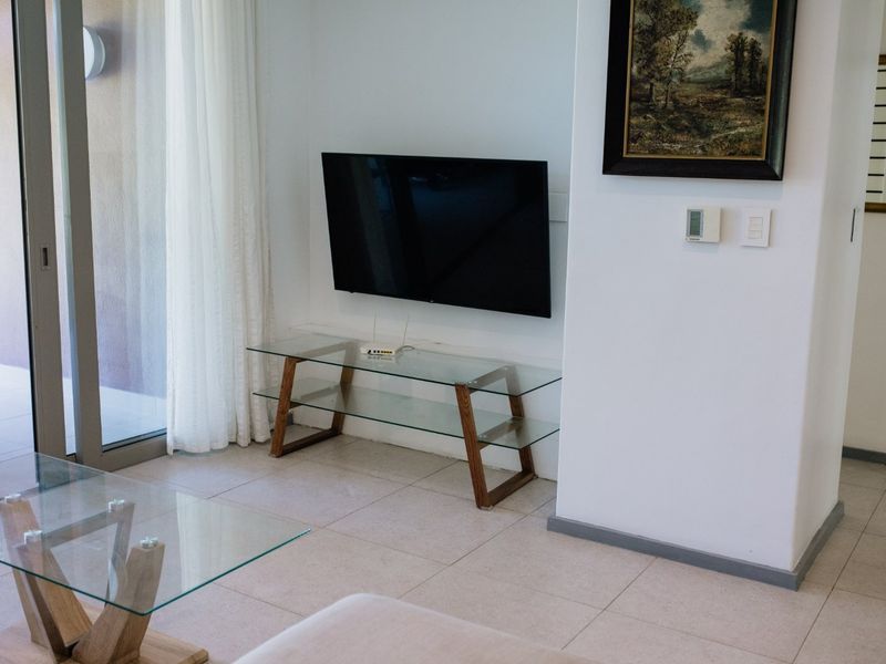 A bright living room featuring tiled flooring, a wall-mounted television, and a large sliding glass door providing access to the outdoor area.