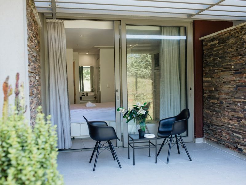 A covered patio area featuring stone-clad walls, tiled flooring, and large sliding glass doors providing access to the interior bedroom.