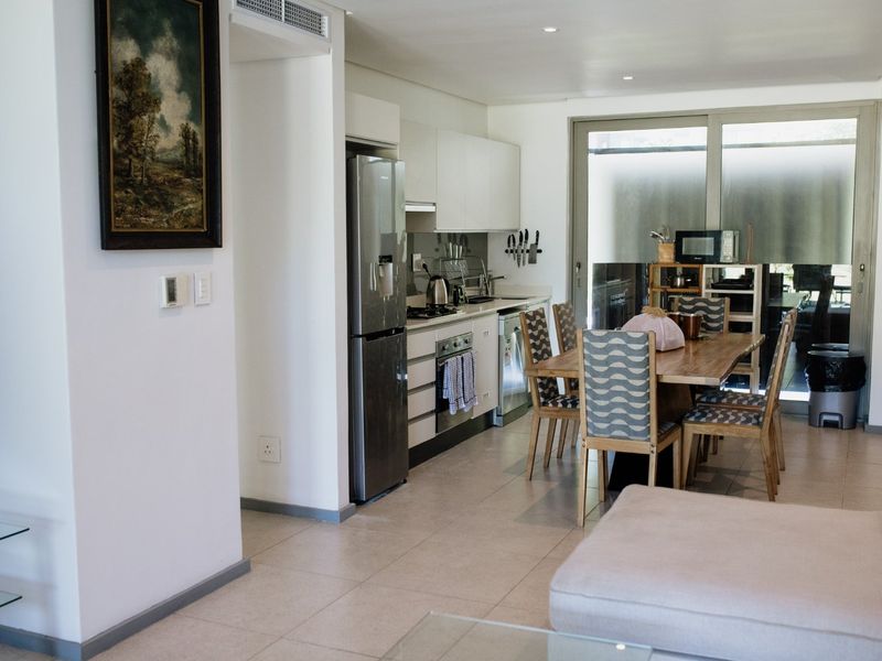 Modern open-plan kitchen and dining area featuring sleek cabinetry, integrated appliances, tiled flooring, and large sliding glass doors leading to an outdoor space.