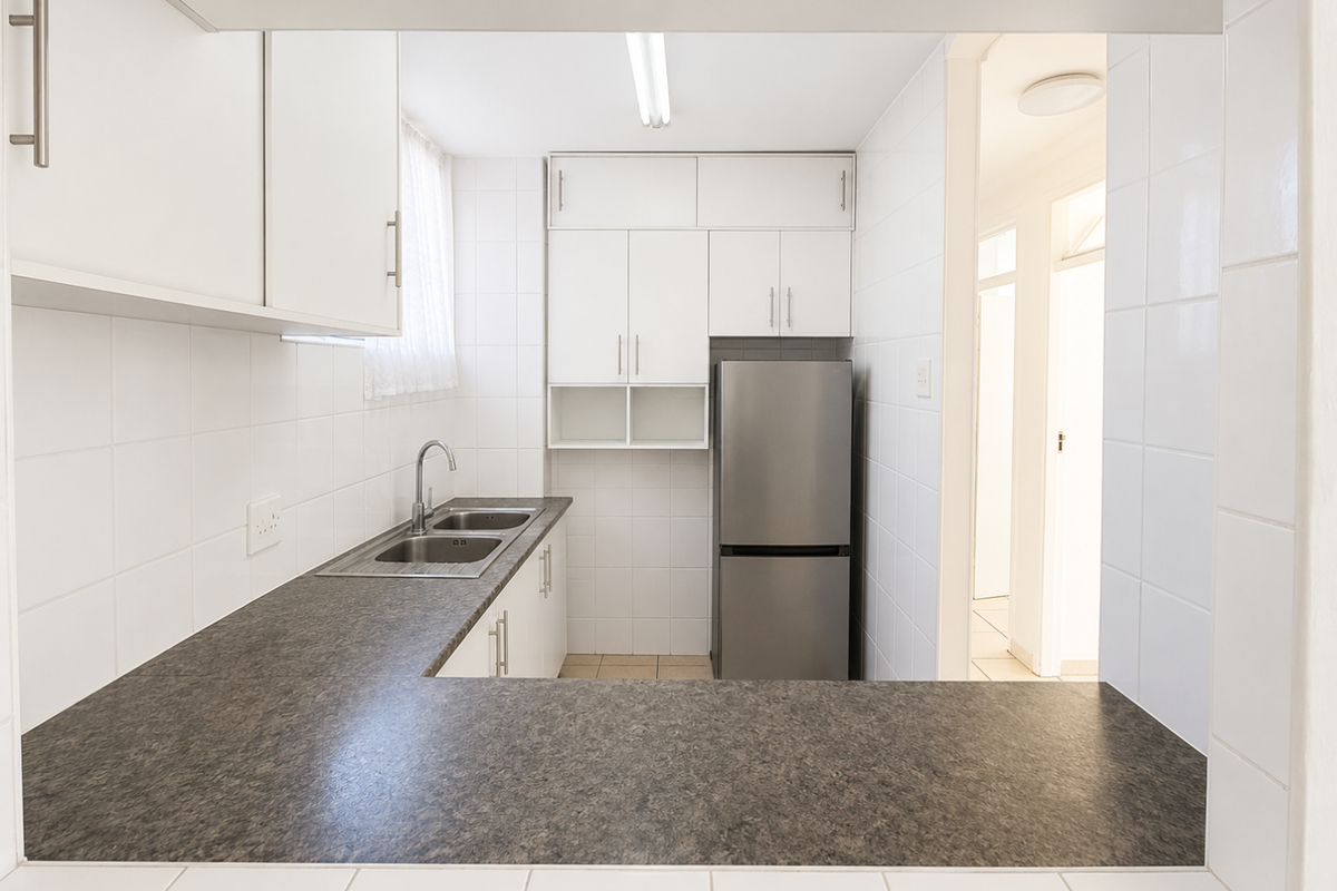 A functional kitchen featuring white cabinetry, dark laminate countertops, a stainless steel sink, and tiled splashbacks, offering a clean and practical workspace.
