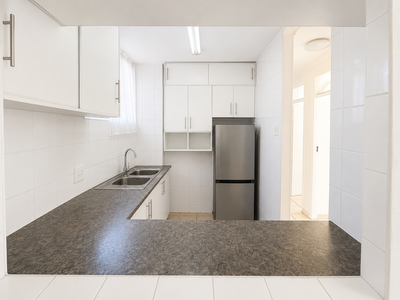 A functional kitchen featuring white cabinetry, dark laminate countertops, a stainless steel sink, and tiled splashbacks, offering a clean and practical workspace.