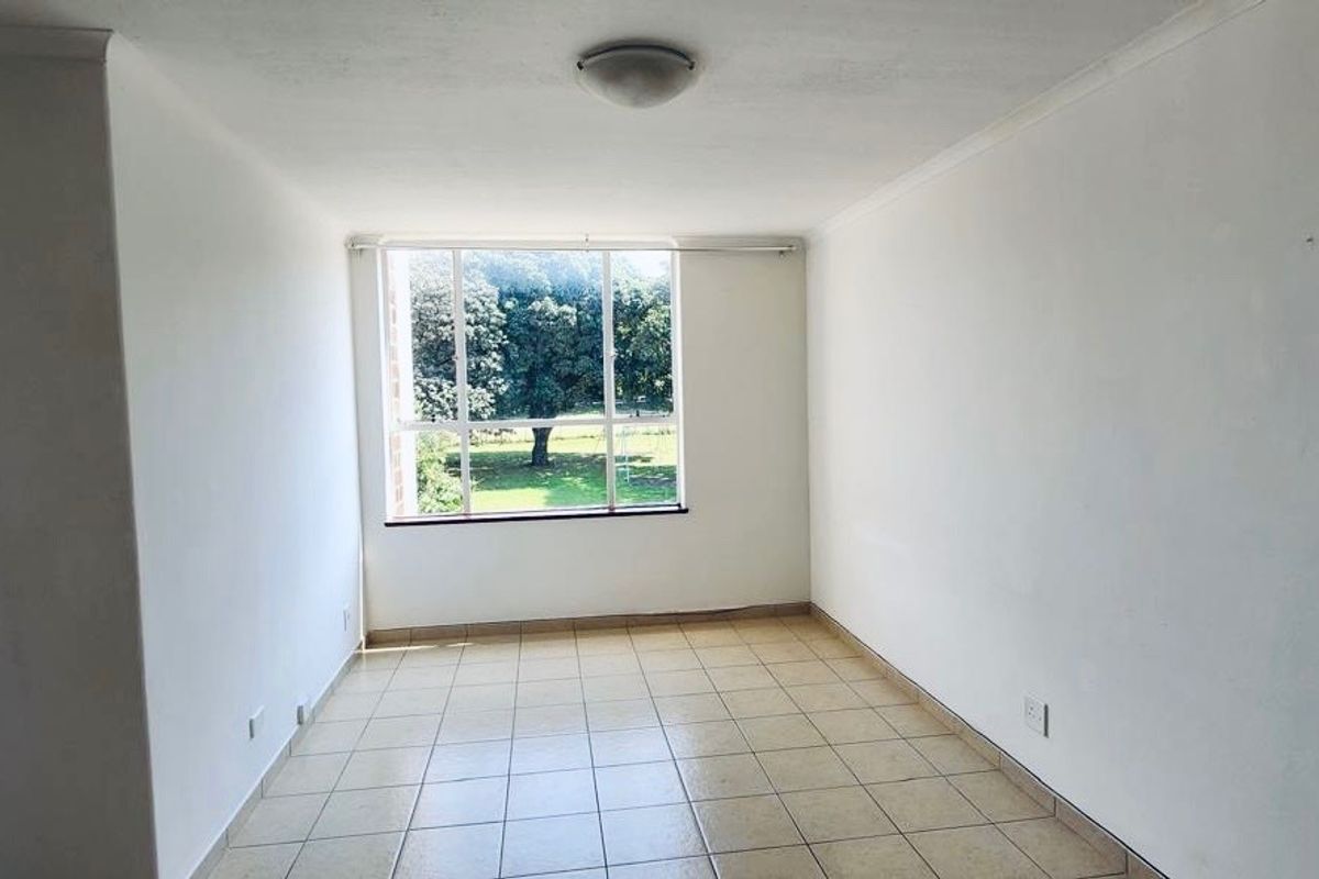 A bright, empty bedroom featuring neutral tiled flooring, a large window with natural light, and a simple ceiling light fixture.