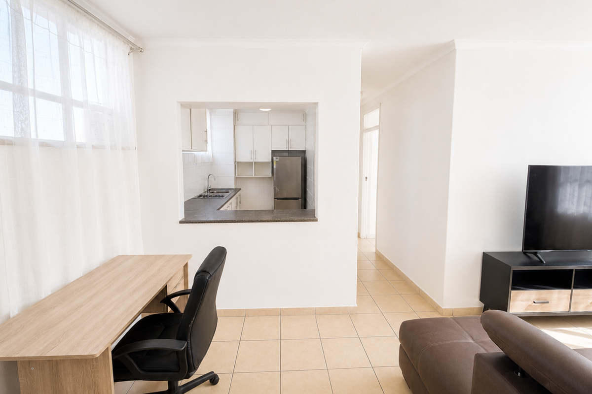 Open-plan living area featuring a functional kitchen pass-through, tiled flooring, and neutral finishes, creating a bright and connected living space.