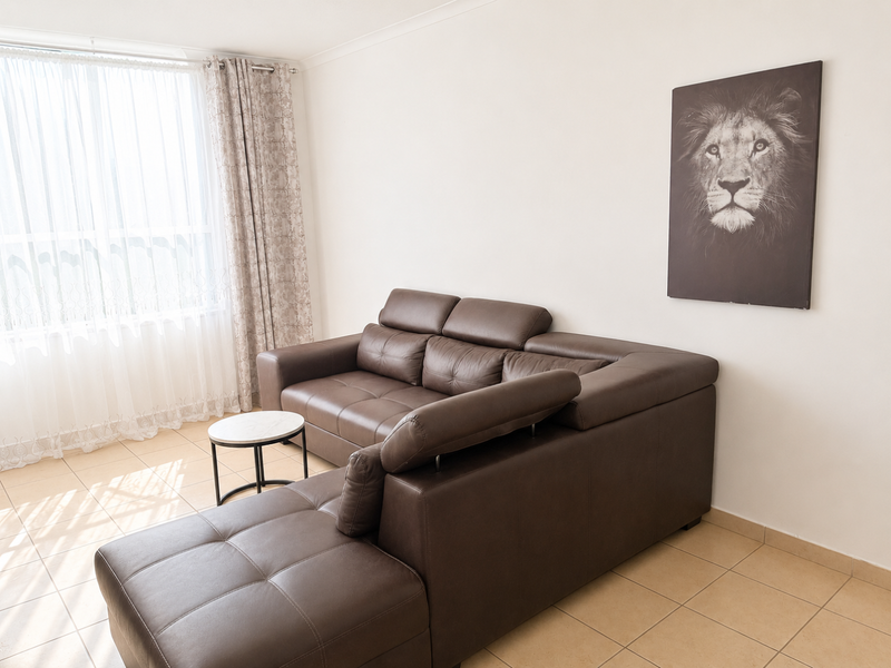 A bright living room featuring neutral tiled flooring and coving, illuminated by natural light through a large window.