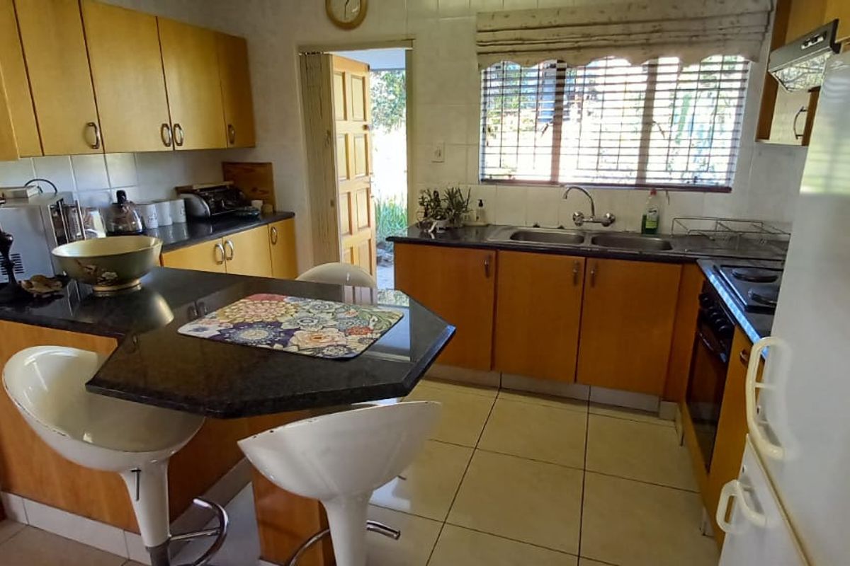 A functional kitchen featuring wooden cabinetry, granite countertops, a breakfast nook, and tiled flooring with direct access to the exterior.