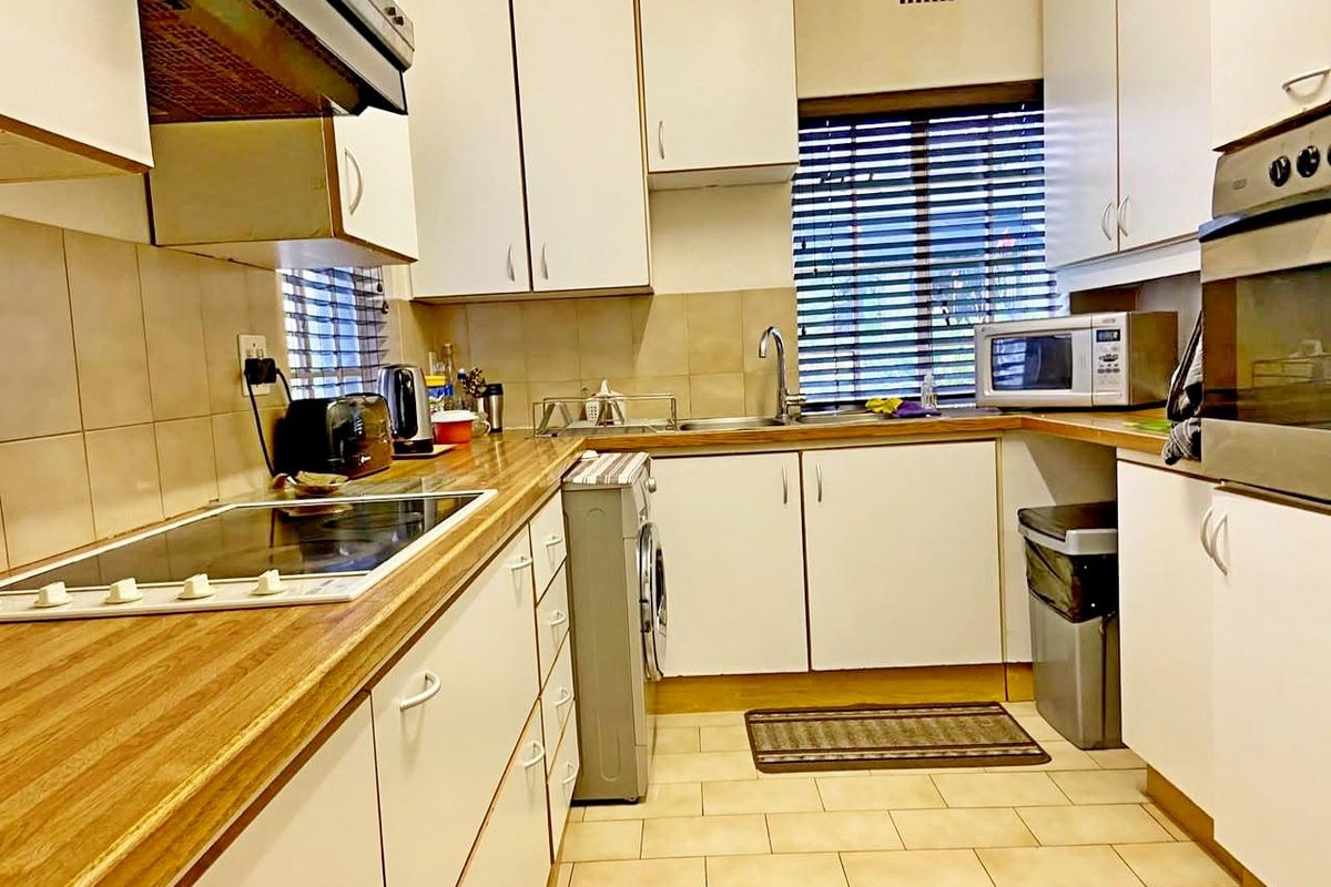 Functional kitchen featuring white cabinetry, wood-look laminate countertops, tiled backsplash, and integrated appliances including an electric hob and oven.