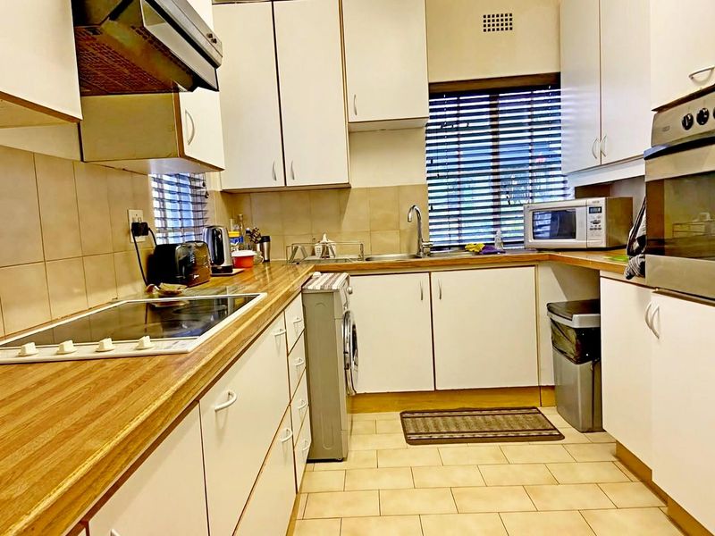 Functional kitchen featuring white cabinetry, wood-look laminate countertops, tiled backsplash, and integrated appliances including an electric hob and oven.