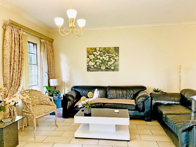 A comfortable living room featuring tiled flooring, classic ceiling cornice, and a central chandelier, providing a neutral base for interior design.