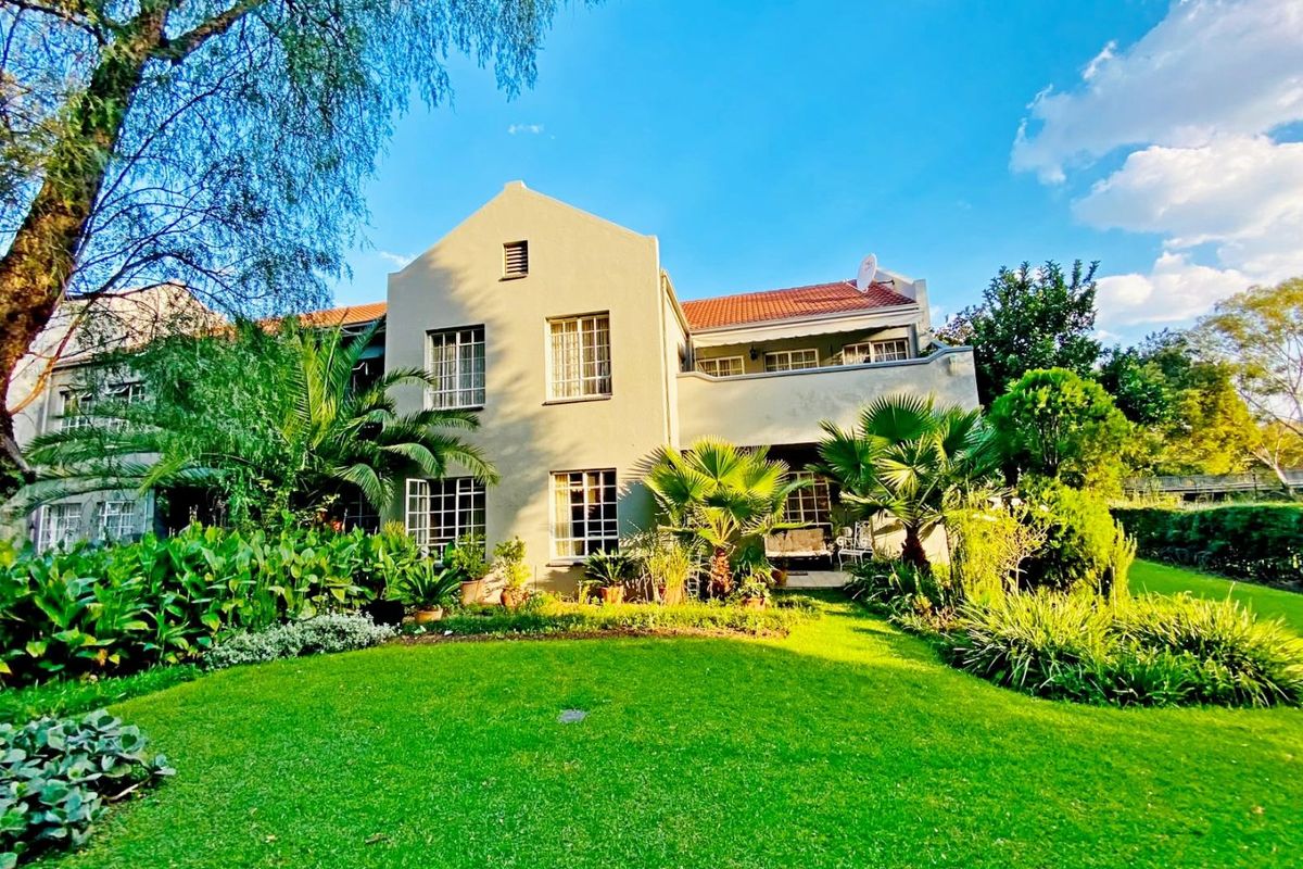 A well-maintained rear elevation of a house featuring a landscaped garden, covered patio area, and classic tiled roof architecture.