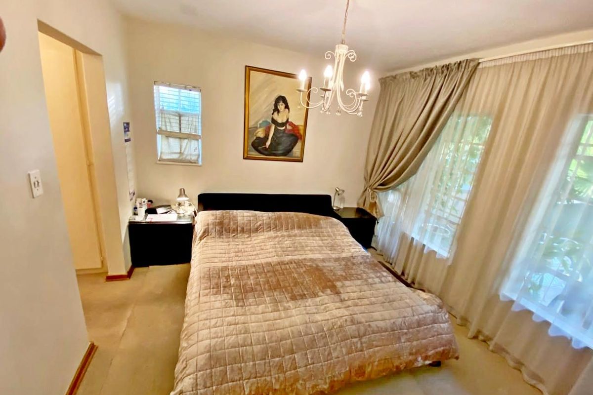 A standard bedroom featuring carpeted flooring, a central chandelier, and large windows with curtain tracks.