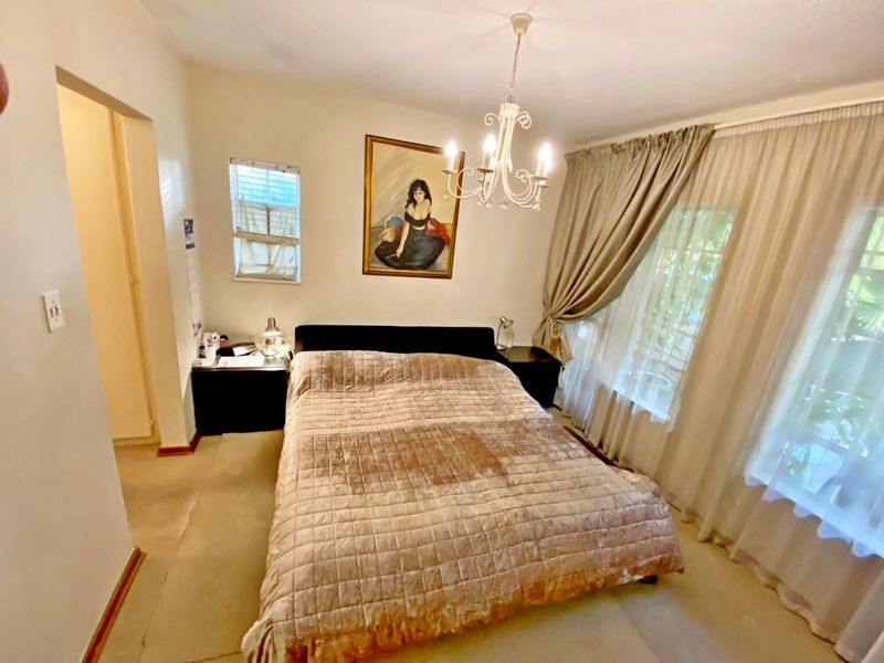 A standard bedroom featuring carpeted flooring, a central chandelier, and large windows with curtain tracks.