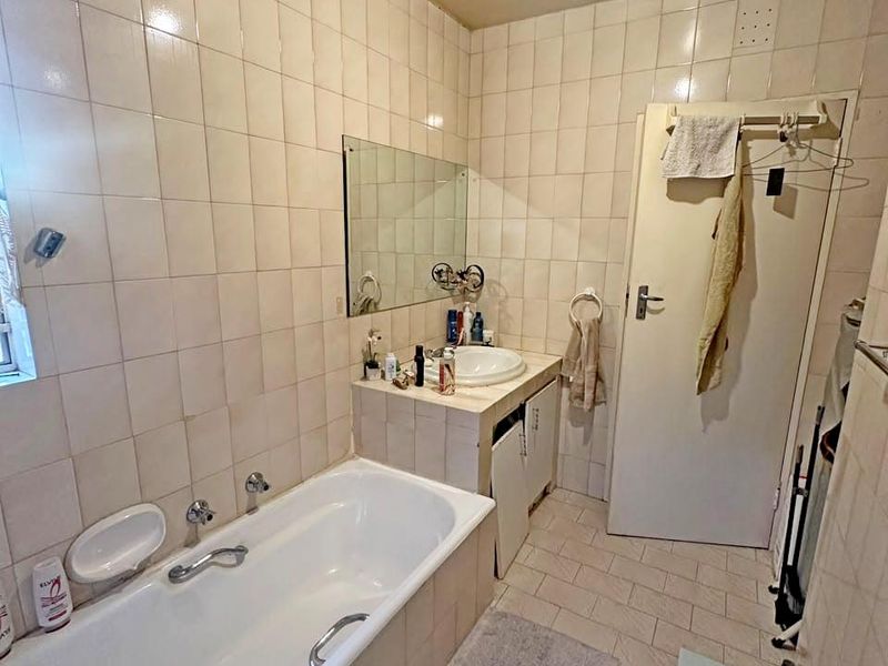 A functional bathroom featuring a built-in bathtub, vanity cabinet, and full-height wall tiling, offering potential for modernization and cosmetic updates.