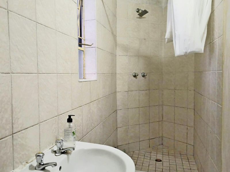 A functional bathroom featuring a wall-mounted basin and a tiled shower enclosure with basic fixtures, requiring cosmetic updates to improve its overall condition.