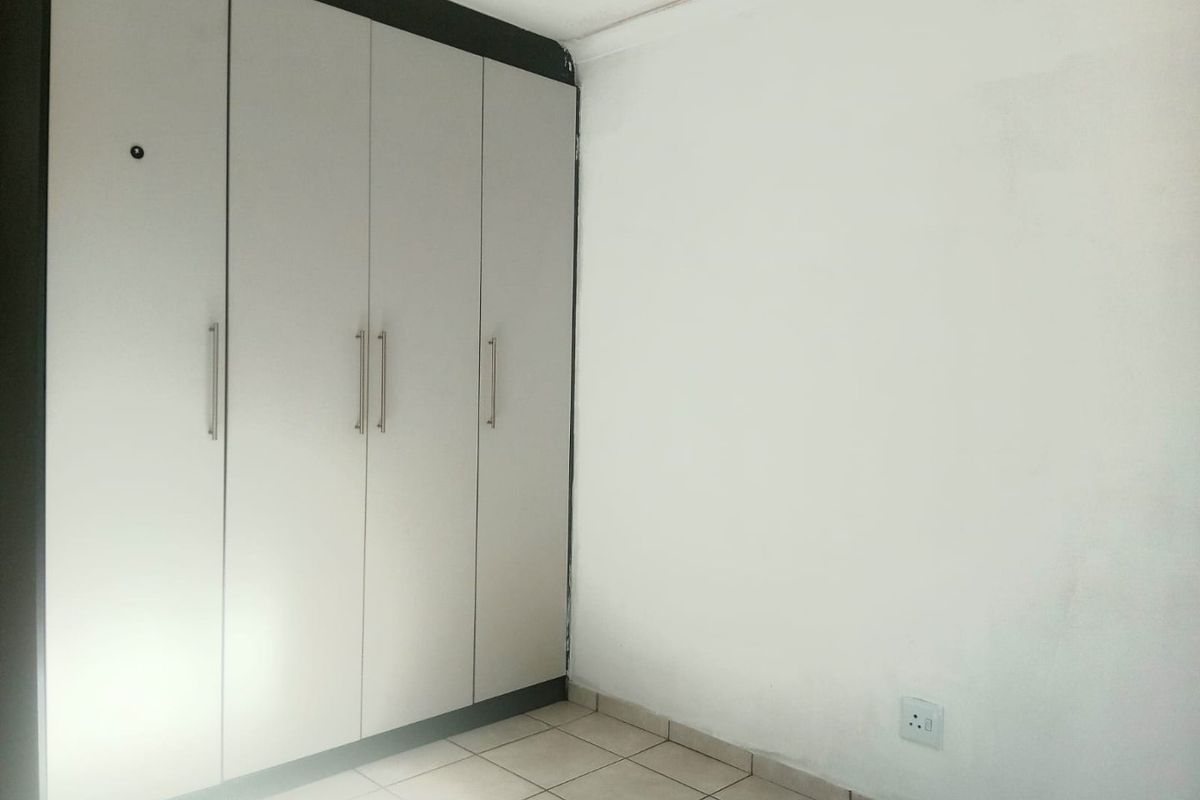 A simple bedroom featuring built-in cupboards and tiled flooring, requiring minor cosmetic updates to the walls and ceiling.