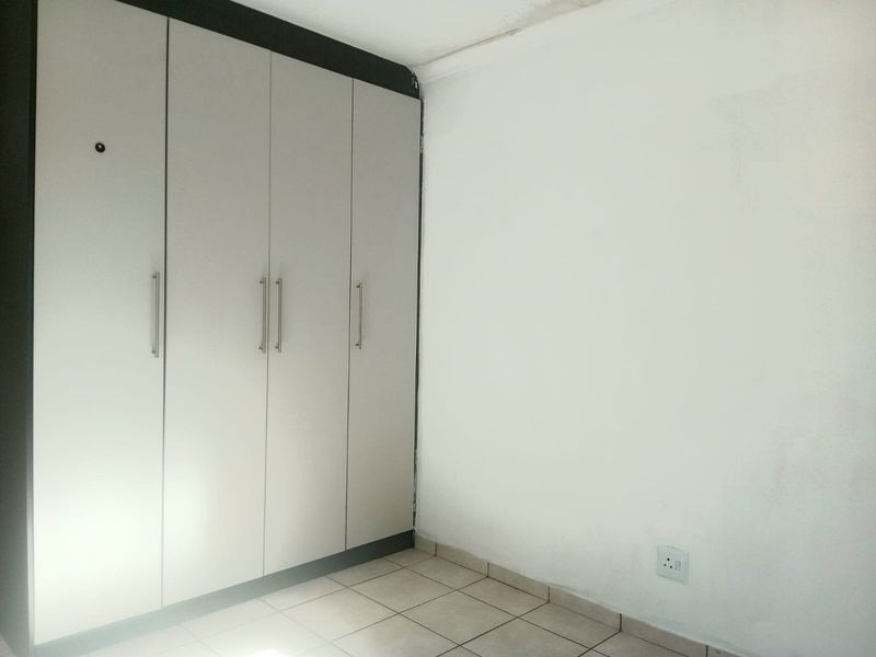 A simple bedroom featuring built-in cupboards and tiled flooring, requiring minor cosmetic updates to the walls and ceiling.