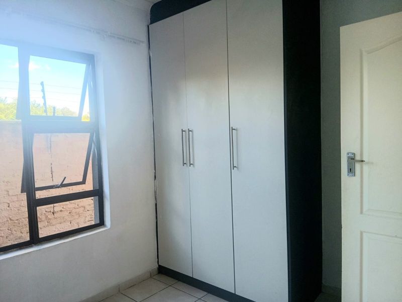 A clean, empty bedroom featuring a modern built-in wardrobe with white doors, tiled flooring, and an aluminium window frame.