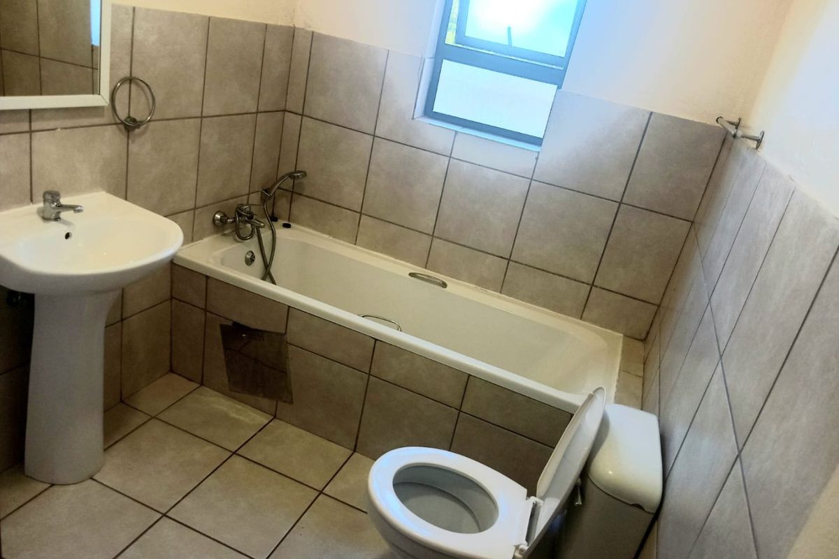 A functional bathroom featuring a pedestal basin, bathtub, and toilet with neutral wall and floor tiling.