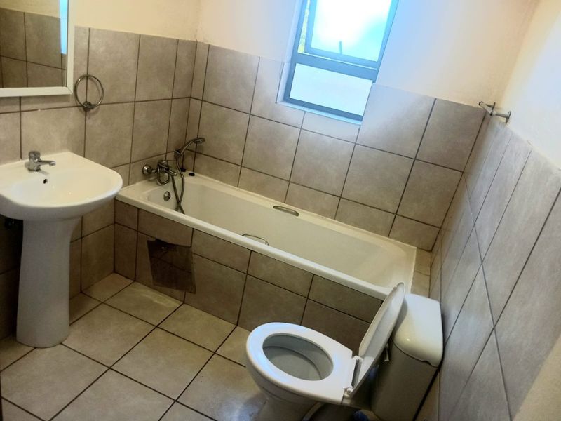 A functional bathroom featuring a pedestal basin, bathtub, and toilet with neutral wall and floor tiling.